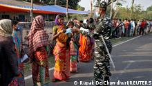 A policeman gives a face mask to a woman as she and others wait in line to cast their vote outside a polling station during the first phase of West Bengal state election in Purulia district, India, March 27, 2021. REUTERS/Rupak De Chowdhuri