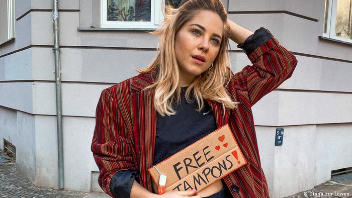 Diana zur Löwen holds a cardboard sign that reads FREE TAMPONS on Instagram
