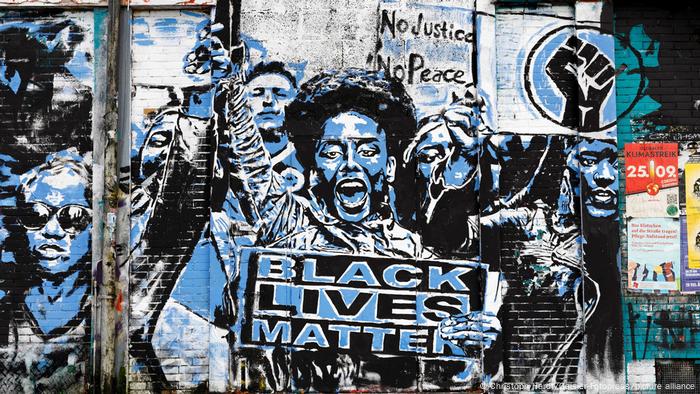 On the wall of a building in Cologne, activists raise their fists in a black and blue painting and hold a Black Lives Matter sign.