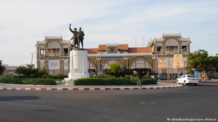 Outside view of train station in Dakar, with low-rise building and colonial statue in front