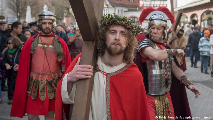In a re-enactment of the Passion of Christ, a man dressed a Jesus carries a cross while being followed by men dressed as Roman soldiers