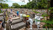 Cemetery workers carry a coffin during the burial of a victim of COVID-19 at the Sao Joao municipal cemetery in Porto Alegre, Brazil, on March 26, 2021. - Brazil surpassed 100,000 new Covid-19 cases in one day on Thursday, adding another grim record in a country where the pandemic has killed more than 300,000 people. (Photo by SILVIO AVILA / AFP) (Photo by SILVIO AVILA/AFP via Getty Images)