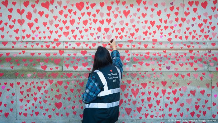 Mulher desenha coração em painel homenageando vítimas da covid no Reino Unido