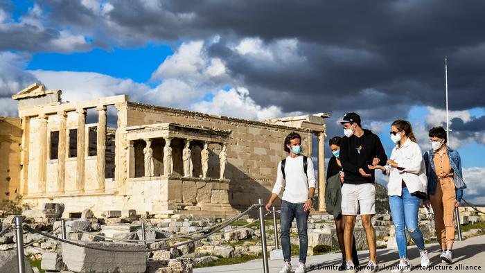 Turistas de máscara com Partenon de Atenas ao fundo