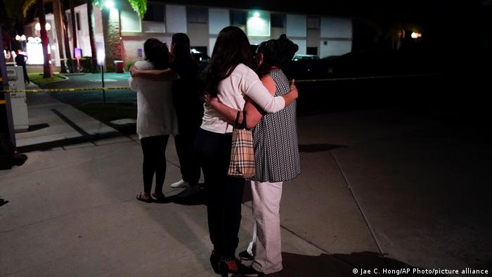 Unidentified people comfort each other as they stand near a business building where a shooting occurred in Orange, California