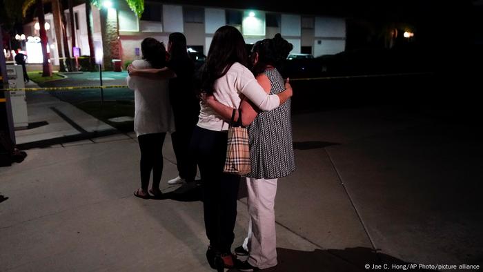 Unidentified people comfort each other as they stand near a business building where a shooting occurred in Orange, California