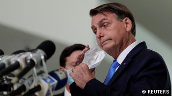 O presidente Jair Bolsonaro tira a máscara em frente a um punhado de microfones durante uma coletiva de imprensa