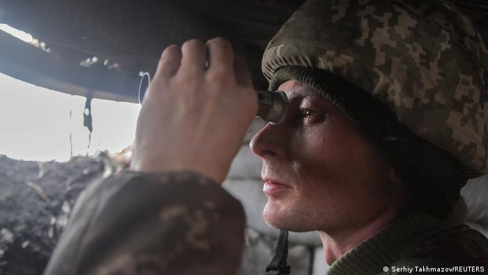 Украинский военный смотрит в бинокль на боевых позициях на линии разъединения недалеко от Донецка