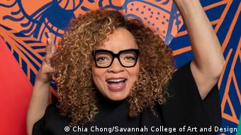 Ruth E. Carter poses against a colorful background.  She laughs broadly, her arms are thrown in the air.