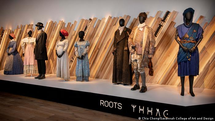 Rows' costumes standing in front of light wood in the exhibition room of the Scandal Atlanta Fashion and Film Museum
