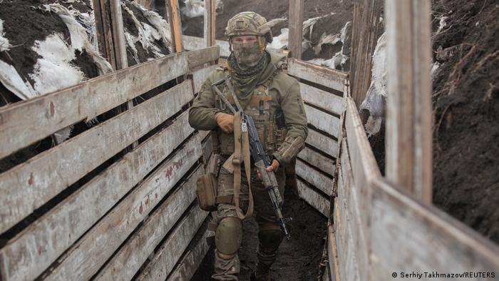 A service member of the Ukrainian armed forces walks in a trench with a rifle