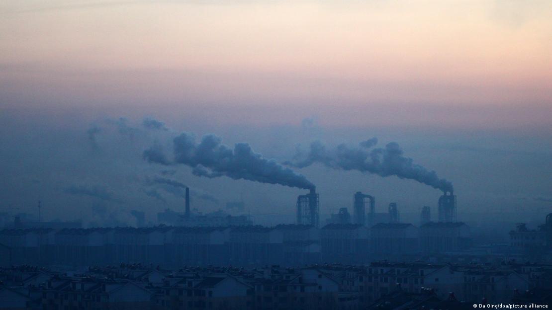 Espessas nuvens de fumaça emanam dos edifícios industriais.