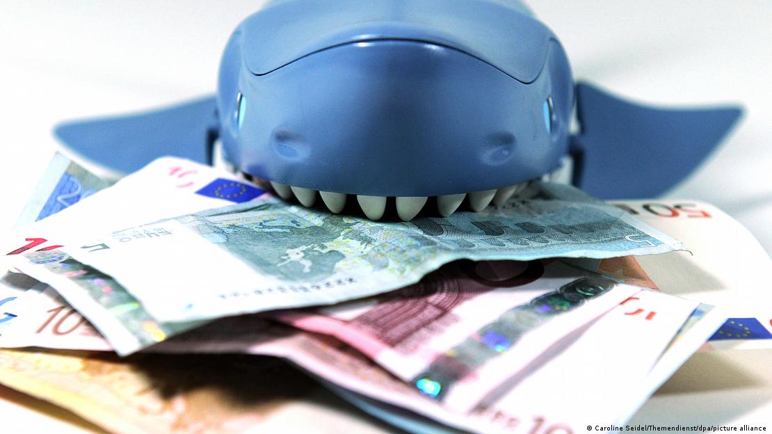 Oyuncak bir köpek balığı euro banknotları üzerinde duruyor. Açık ağzındaki dişler banknotlara uzanıyor