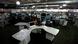 The image shows the newsroom of the Venezuelan newspaper El Nacional, with numerous desks, computers, and several journalists at work.