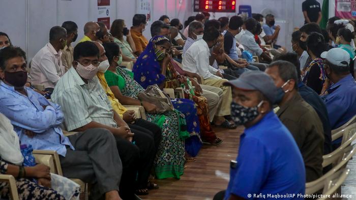 Pessoas de máscara aguardam sentadas em centro de vacinação na Índia