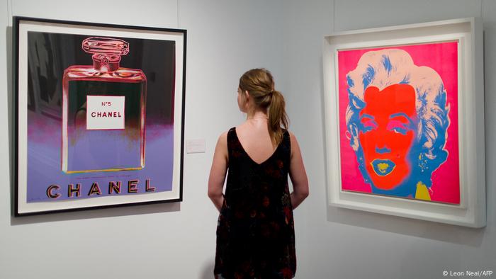 A gallery assistant poses between US artist Andy Warhol's 1985 ADS: CHANEL and 1967 Marilyn.
