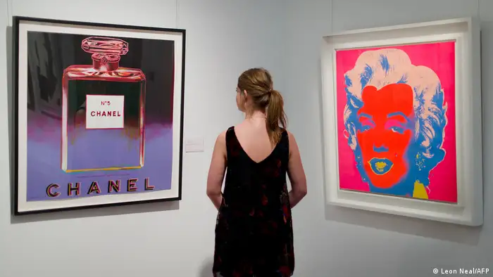 A gallery assistant poses between US artist Andy Warhol's 1985 ADS: CHANEL (left) and 1967 Marilyn (Right) at Sotheby's auction house in London.