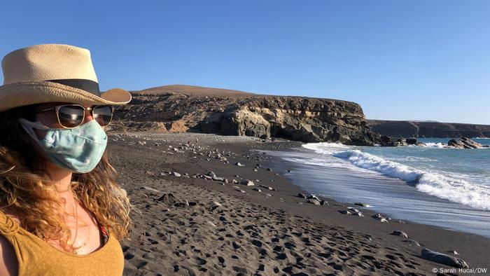 Una mujer con gafas de sol y una máscara se encuentra junto al mar en una playa de la isla de Fuerteventura.