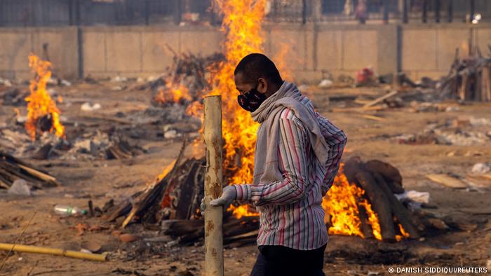 A man walks past burning funeral pyres of people, who died of COVID-19 at a crematorium ground in New Delhi