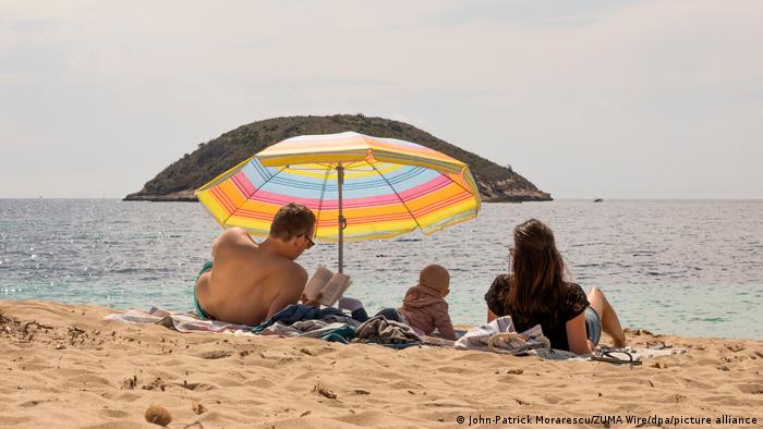 A family on a beach under a parasol looking out at the sea, Spain