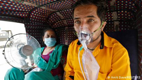 A patient wearing an oxygen mask looks on as his wife holds a battery-operated fan while waiting inside an auto-rickshaw to enter a COVID-19 hospital for treatment