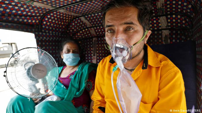 A patient wearing an oxygen mask looks on as his wife holds a battery-operated fan while waiting inside an auto-rickshaw to enter a COVID-19 hospital for treatment