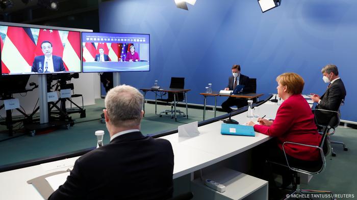 Chanceler federal alemã, Angela Merkel, e outros políticos sentados a mesa longa, diante de monitores de televisão