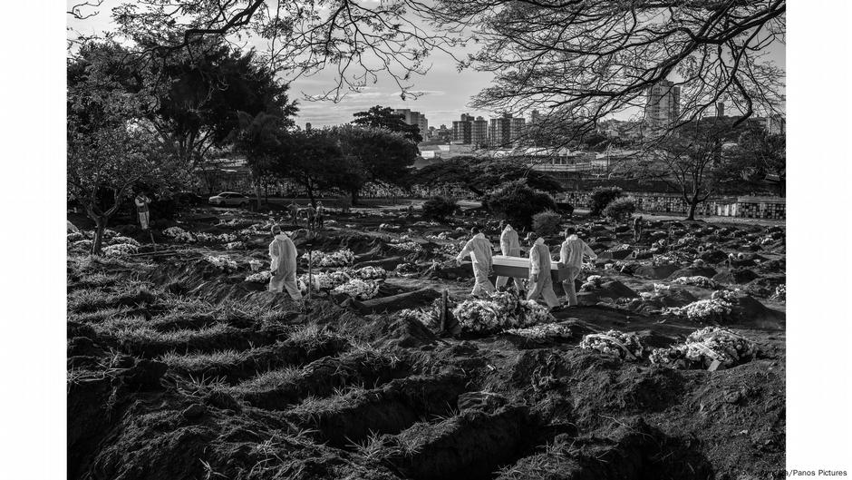 White-clad workers carrying coffin at cemetery amid dug graves. Photo: Lalo de Almeida, Brazil