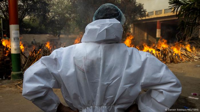 Pessoa de veste protetora de costas observa fogueiras de cremação