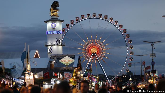 Evening view of the Oktoberfest festival with beer people mingling among beer tents and ferris wheel