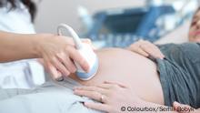 Close up of incognito professional doctor using ultrasound equipment, screening of pregnant woman. Doctor in white uniform touching stomach by tool of young female, who lying on bed at cabinet.