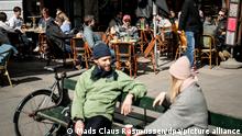 Menschen sitzen zur heute erwirkten Wiedereröffnung von Bars und Cafés bei Sonnenschein im belebten Außenbereich eines Cafés. +++ dpa-Bildfunk +++