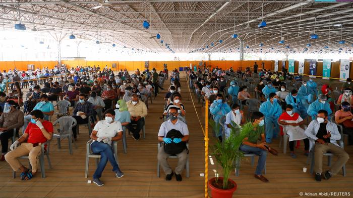 A large crowd sits spaced apart in a waiting room awaiting vaccination against COVID