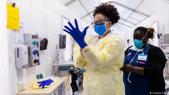 Fotoausstellung Faces of Resilience: Eine Ärztin mit Mundschutz streift einen Handschuh über, eine Schwesterschnürt ihren Schutzanzug zu