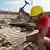 Ein Bauarbeiter im roten T-Shirt und mit gelbem Helm auf dem Kopf schwingt auf einem Baugerüst den Hammer (Foto: dpa)