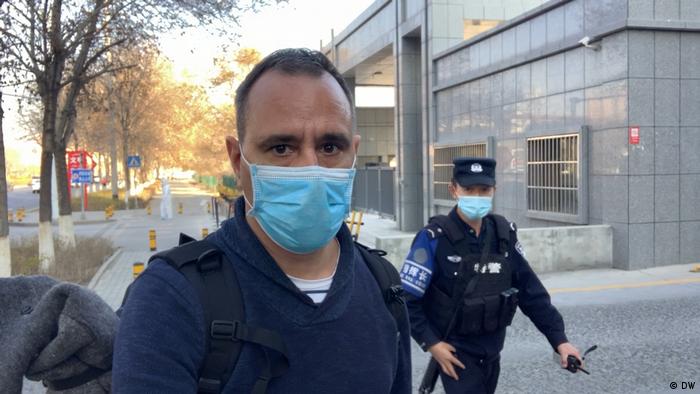 Mathias Bölinger in Beijing, man wearing face mask looks into camera, policeman in the background