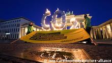 Greenpeace-Aktivisten mit brennenden CO2-Buchstaben und einem Protestbanner vor dem Brandenburger Tor