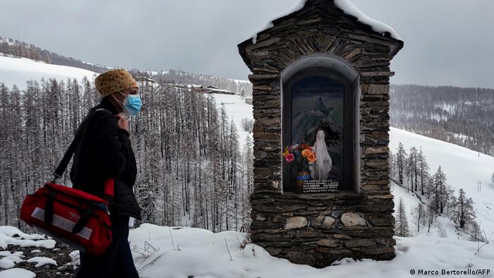 Medical personnel wearing face masks walk behind a small altar in the snow