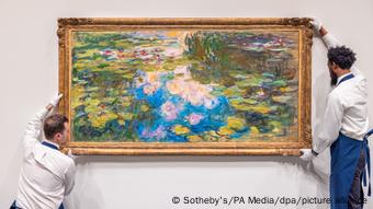 Zwei Männer halten das Gemälde Seerosenteich bei Sotheby's in New York. Sie tragen weiße Handschuhe.