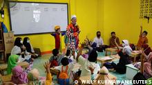 Yahya Edward Hendrawan, a 38-year-old Indonesian teacher who dresses up as a clown to conduct classes, and his 5-year-old son Mirza, dressed up as a baby clown, stand among students during a class at a boarding school in Tangerang, Banten province, Indonesia, April 21, 2021. Picture taken April 21, 2021. REUTERS/Willy Kurniawan