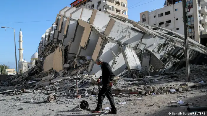 A man with a walking stick passes by a destroyed building