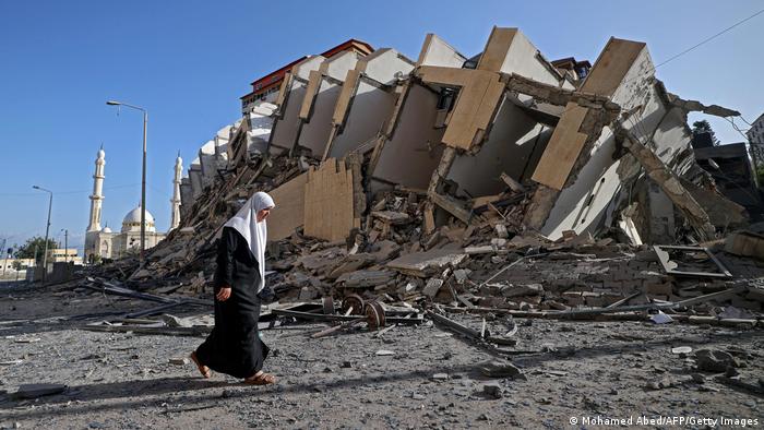 Mulher caminha ao lado de destroços de edifício destruído por ataque israelense em Gaza