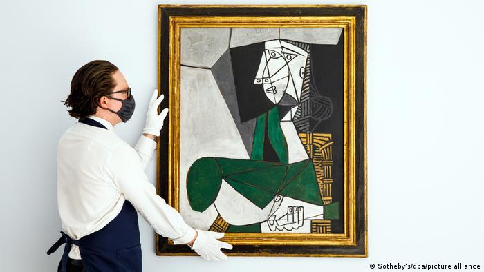Ein Mann mit Mundschutz hängt das Picasso-Gemälde Femme assise en costume auf
