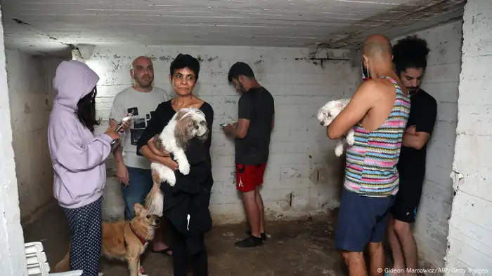 Six people and three dogs wait in a walled room with a low ceiling.