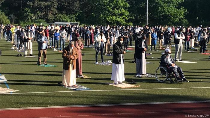 Auf einem Sportplatz stehen bei Sonnenschein Männer auf Gebetsteppichen