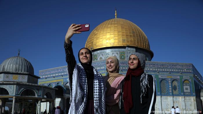 Drei Musliminnen stehen nebeneinander vor der goldenen Kuppel des Felsendoms, eine hält ihr Handy hoch und macht ein Foto von sich und den anderen beiden.