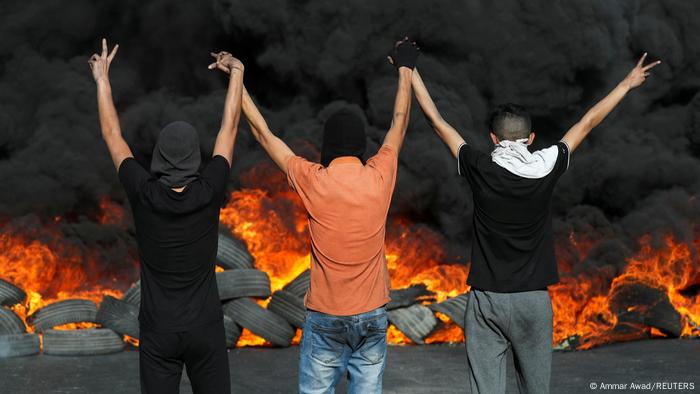 Three men seen from the back raising their arms before a pile of burning tires Three men seen from the back raising their arms before a pile of burning tires
