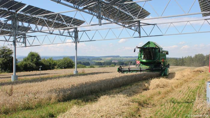 A farm vehicle moves toward a part of the field that stands under solar panels