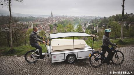 Der Bestatter Gyan Härri ist mit dem Bestattungsfahrrad und einem offen sichtbaren Sarg unterwegs. Begleitet wird er von einer Mitarbeiterin.