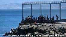 Polizisten überwachen Mitgranten aus Marokko, die über den See in der Nähe des Zauns von Ceuta an Land gekommen sind. +++ dpa-Bildfunk +++